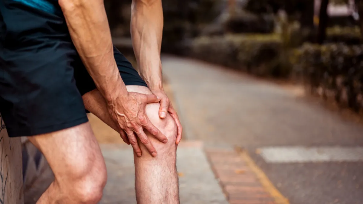 Runner gripping their knee in pain at the roadside Runner gripping their knee in pain at the roadside