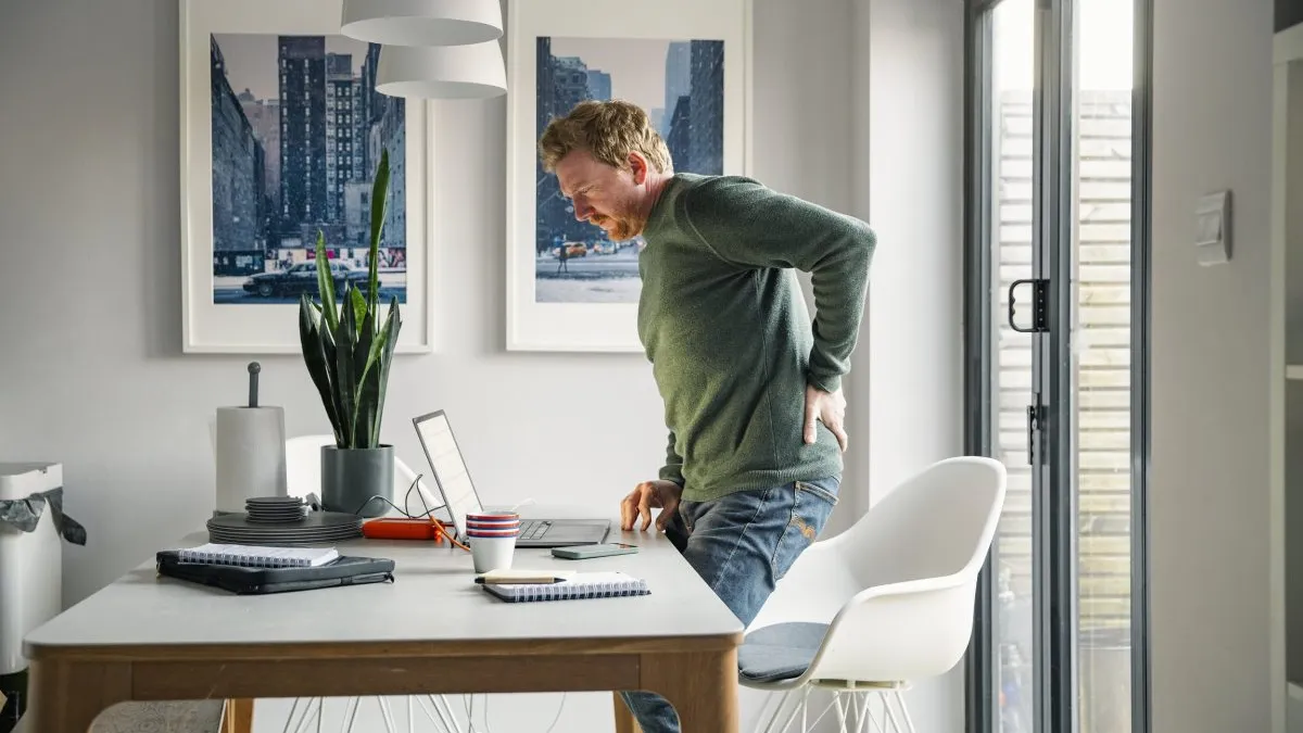 Man stretching at a standing desk beside a window at home